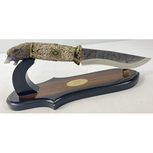 1174 - An ornamental survival style knife with display stand (a/f). Resin handle in the shape of a wolfs he... 