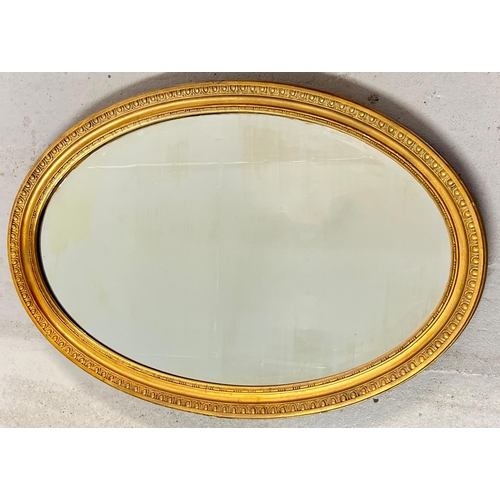 1445 - A large oval shaped gilt framed wall mirror with bevel edged glass. Approx. 61cm x 91cm.