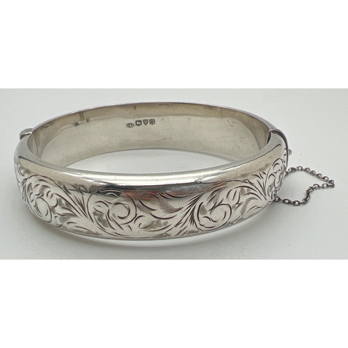 1005 - A vintage silver bangle with floral design engraving throughout, push clasp and safety chain. 1.5 cm... 