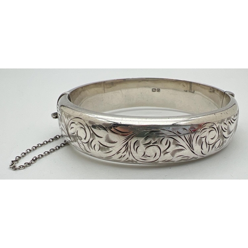 1005 - A vintage silver bangle with floral design engraving throughout, push clasp and safety chain. 1.5 cm... 