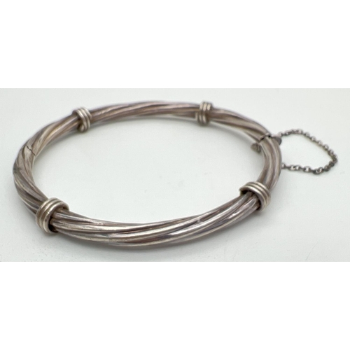 1015 - A twist design silver bangle with push clasp and safety chain. Silver marks to clasp. Approx 7cm acr... 