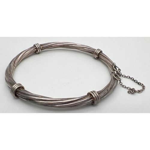 1015 - A twist design silver bangle with push clasp and safety chain. Silver marks to clasp. Approx 7cm acr... 