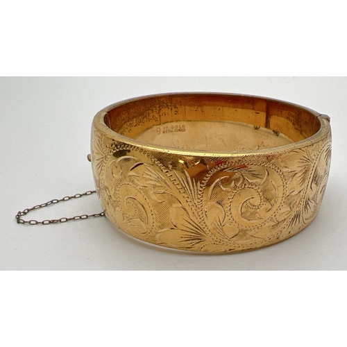 1024 - A vintage 9ct gold metal core hinged bangle with half floral engraved pattern, push clasp & safety c... 