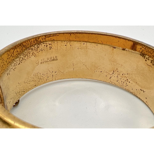 1024 - A vintage 9ct gold metal core hinged bangle with half floral engraved pattern, push clasp & safety c... 