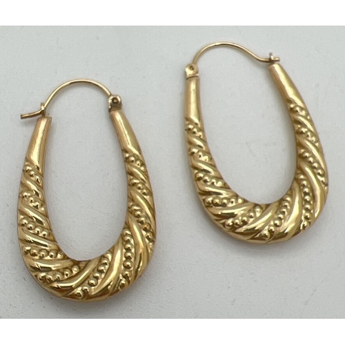 1064 - A pair of 9ct gold oval shaped hoop style earrings with twist beaded pattern. Hinged posts. Marked 9... 