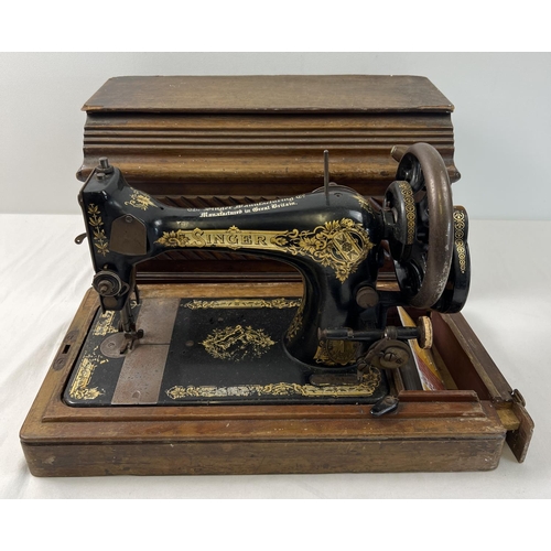 1408 - A vintage Singer hand crank sewing machine, in wooden case. Painted black with gilt floral decoratio... 