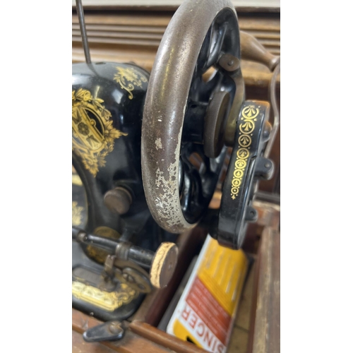 1408 - A vintage Singer hand crank sewing machine, in wooden case. Painted black with gilt floral decoratio... 