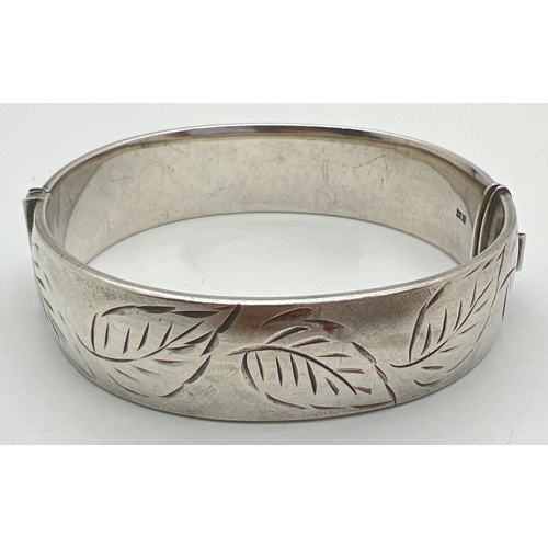 1092 - A vintage silver bangle with half engraved leaf decoration and slide push clasp. Hallmarked to insid... 