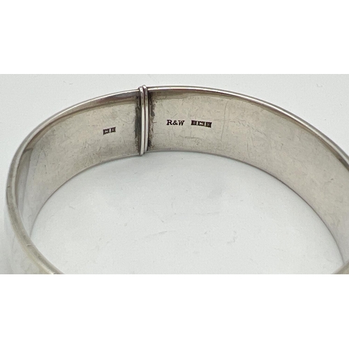 1092 - A vintage silver bangle with half engraved leaf decoration and slide push clasp. Hallmarked to insid... 