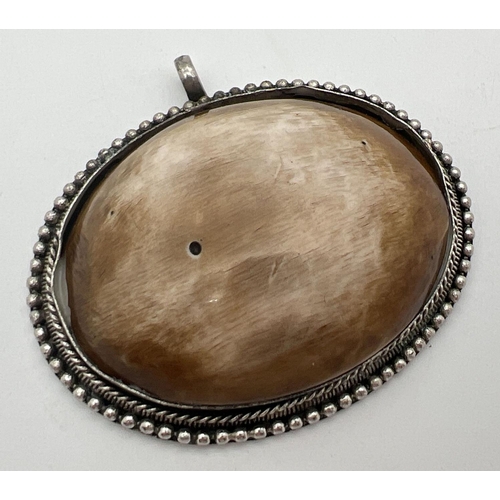 1097 - A large oval pendant set with a large brown and cream coloured shell in a beaded edged white metal m... 