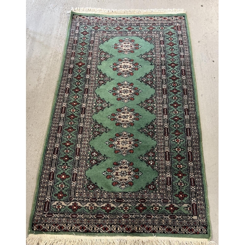 1495 - A small green ground Persian rug with beige, black and red design and tassled ends. Approx. 160cm x ... 