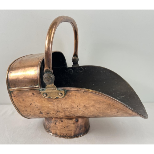 1200 - A Victorian copper and brass helmet fireside coal scuttle with hinged swing handle. Raised on a cyli... 