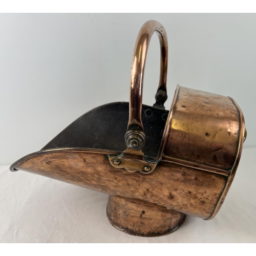 1200 - A Victorian copper and brass helmet fireside coal scuttle with hinged swing handle. Raised on a cyli... 