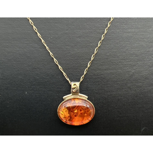 63 - A silver and 18ct gold accent amber set oval pendant with spiral detail to bale on a 18ct gold 18 in... 