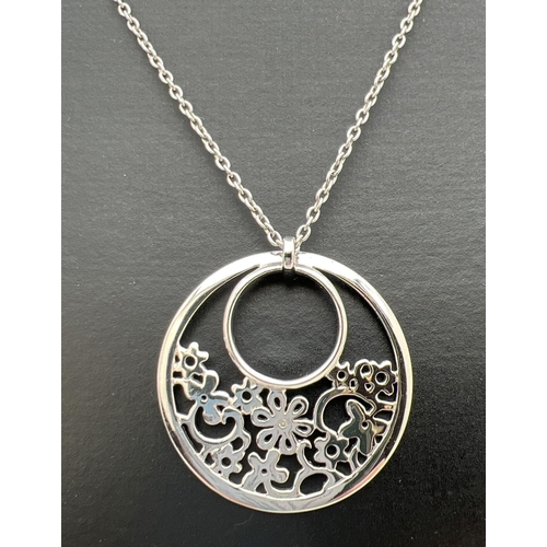 217 - A silver circular shaped pendant with pierced work floral design set with a single small diamond, by... 