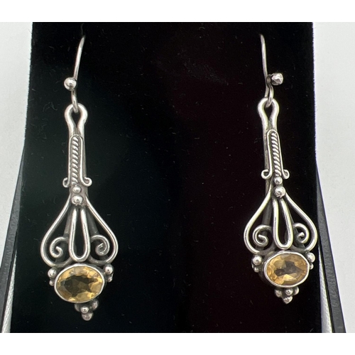 268 - A pair of white metal Gothic style drop earrings, each set with an oval cut Citrine stone. Bezel set... 