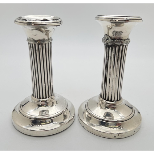 1115 - A pair of early 20th century silver covered candlesticks with chanelled design stems and stepped fee... 