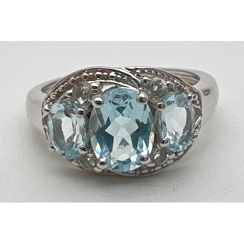 1015 - A silver and topaz trilogy dress ring, set with 3 oval cut blue topaz stones in an illusion halo set... 
