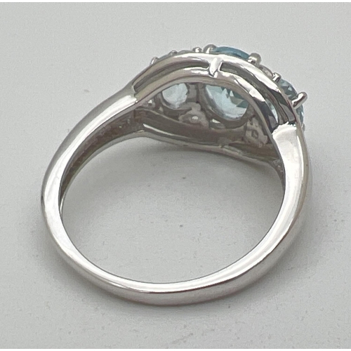 1015 - A silver and topaz trilogy dress ring, set with 3 oval cut blue topaz stones in an illusion halo set... 