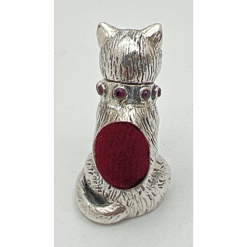 1123 - A small silver pin cushion modelled as a cat with green stone set eyes and red stone set collar. Sta... 