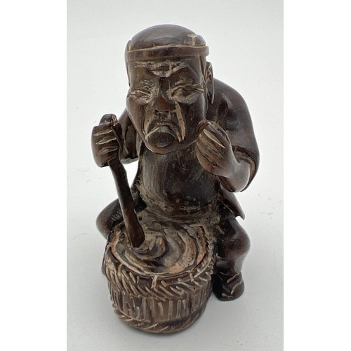 1212 - A carved wooden netsuke modelled as a man stirring a pot. Set with small mother of pearl disc to und... 