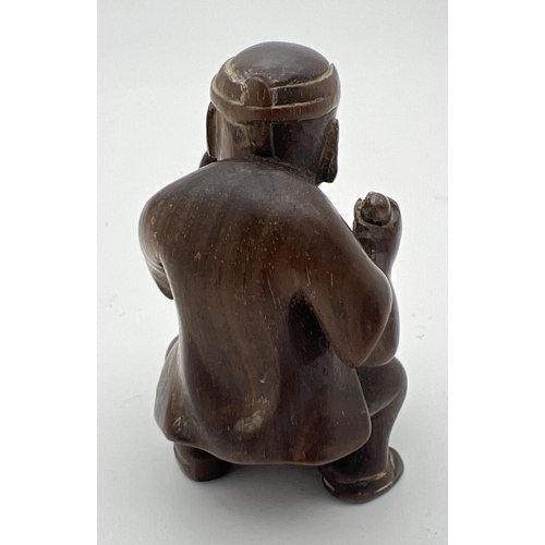 1212 - A carved wooden netsuke modelled as a man stirring a pot. Set with small mother of pearl disc to und... 