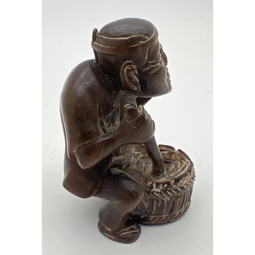 1212 - A carved wooden netsuke modelled as a man stirring a pot. Set with small mother of pearl disc to und... 