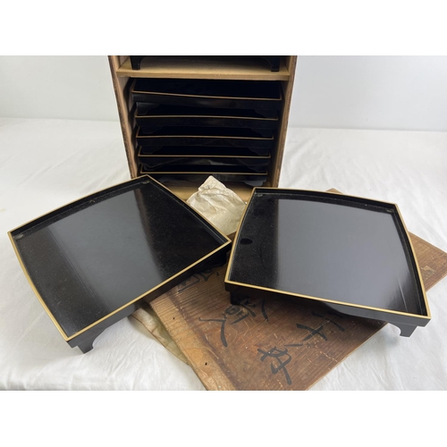 1216 - A collection of 10 Japanese black lacquer footed stands/trays in a wooden box with Chinese lettering... 