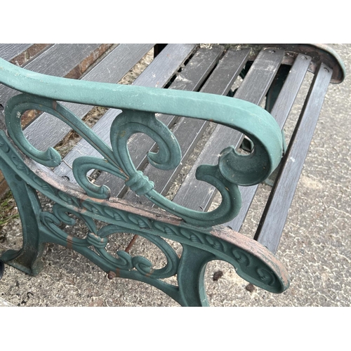 1512 - A wooden slatted garden seat and matching footstool/side table, with cast iron ends. Painted green w... 