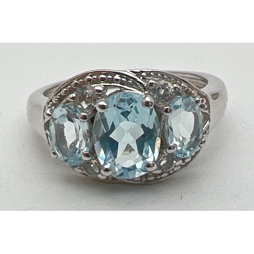 1110 - A silver and topaz trilogy dress ring, set with 3 oval cut blue topaz stones, in an illusion halo se... 