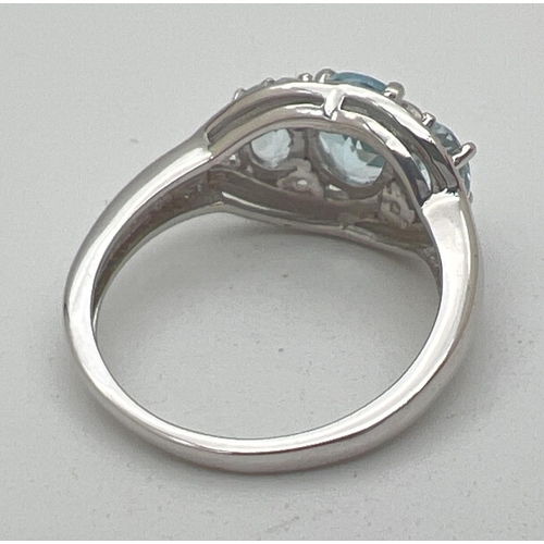 1110 - A silver and topaz trilogy dress ring, set with 3 oval cut blue topaz stones, in an illusion halo se... 