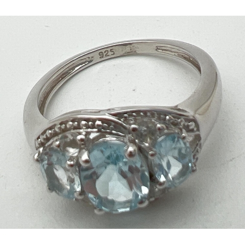 1110 - A silver and topaz trilogy dress ring, set with 3 oval cut blue topaz stones, in an illusion halo se... 