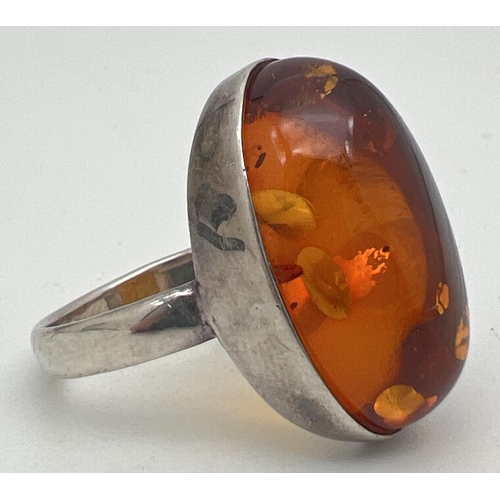 1015 - A large silver dress ring set with an oval cut amber cabochon. Ring size S. Silver mark to inside of... 