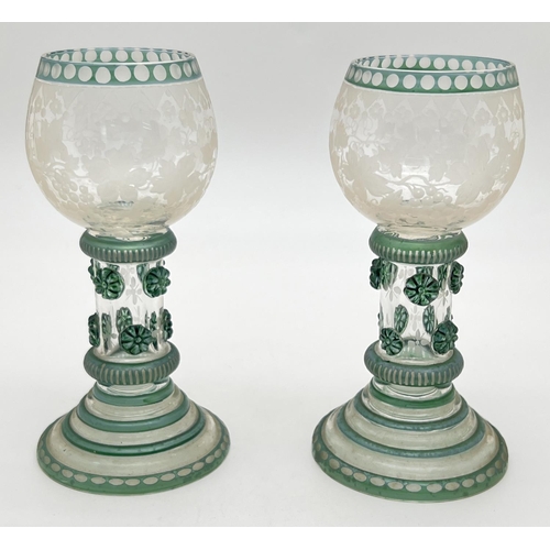 A pair of antique European roemer wine glasses with green tinted detail and grape & vine etched design to bowls. Hollow stem and foot with floral punts. One glass has a small chip to underside of foot rim. Each approx. 16cm tall.