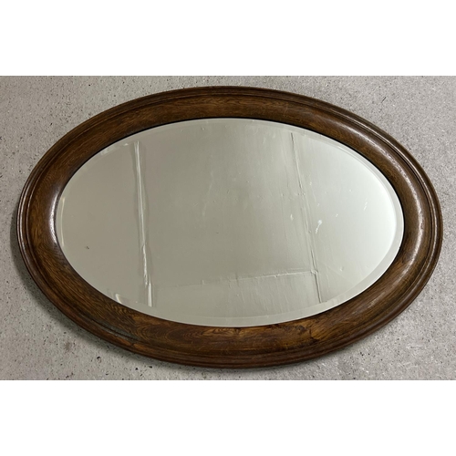 1428 - A vintage dark oak framed oval shaped hall mirror with bevel edged glass. Approx. 86.5cm x 62cm.