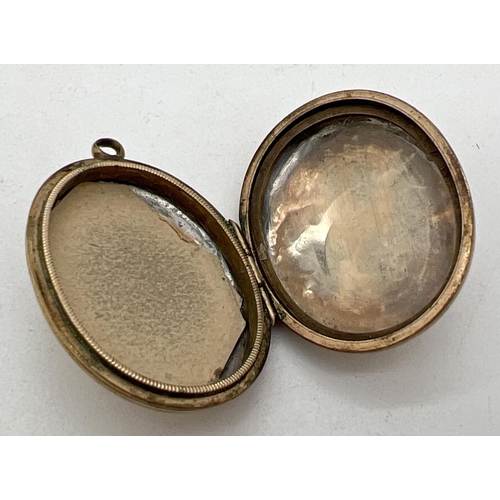 1084 - A yellow metal (front and back) oval locket with floral decoration to front and foliate & scroll eng... 