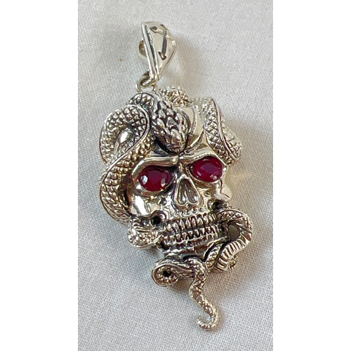 1076A - An unmarked white metal pendant in the form of a skull with a snake, set with rubies for eyes. Appro... 