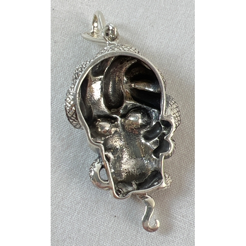 1076A - An unmarked white metal pendant in the form of a skull with a snake, set with rubies for eyes. Appro... 