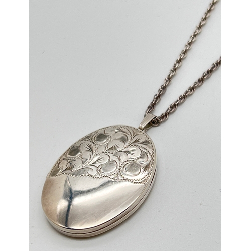 1013 - A large vintage silver oval shaped locket with half engraved detail of scroll & foliate design. On a... 