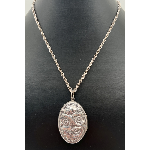 1026 - A large oval silver locket with floral design in relief to front. On a 20