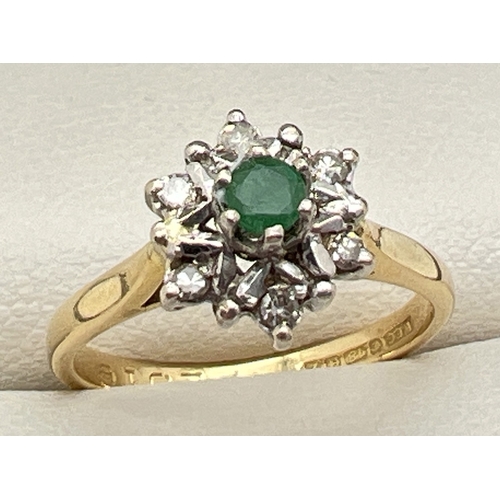 An 18ct gold, emerald and diamond dress ring. High set central round cut emerald surrounded by 6 illusion set round cut diamonds. Full hallmarks to inside of band. Ring size K½. Total weight approx. 3.2g.