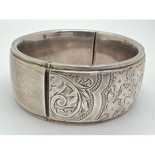 1020 - A vintage silver bangle with push clasp and half floral engraved decoration. Silver marks to inside ... 