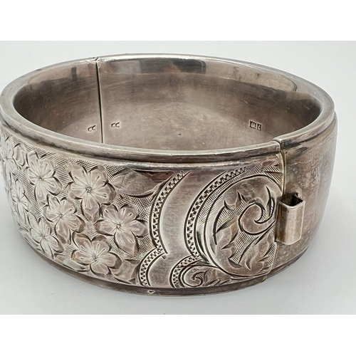 1020 - A vintage silver bangle with push clasp and half floral engraved decoration. Silver marks to inside ... 