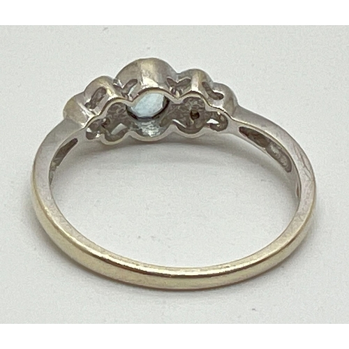 1004 - A 9ct white gold bezel set aquamarine and diamond dress ring. Central oval cut aquamarine with 3 sma... 