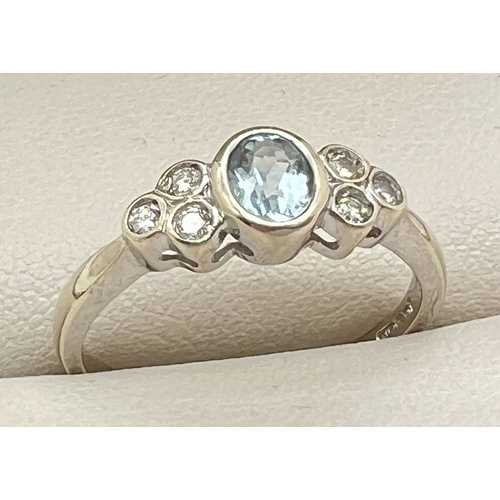 1004 - A 9ct white gold bezel set aquamarine and diamond dress ring. Central oval cut aquamarine with 3 sma... 