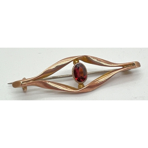 1002 - A 9ct gold brooch of twist design set with central oval cut garnet stone. Marked '9ct' to reverse. A... 