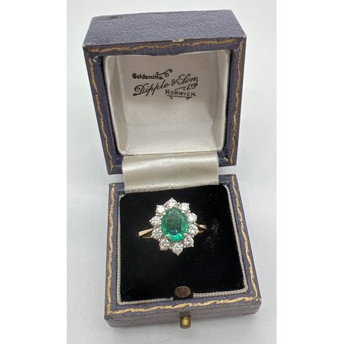 1157 - An 18ct gold, emerald and diamond cluster ring. A central oval cut emerald surrounded by 10 round cu... 