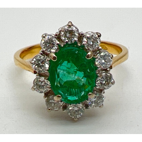 1157 - An 18ct gold, emerald and diamond cluster ring. A central oval cut emerald surrounded by 10 round cu... 