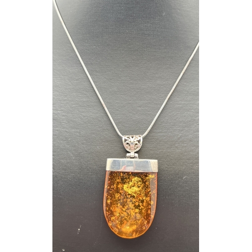 1043 - A modern design large amber pendant with silver cap and pierced work bale. Silver mark to top of cap... 