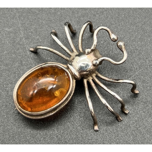 1047 - A silver and amber spider shaped brooch set with an oval amber cabochon. Silver mark to underside. A... 